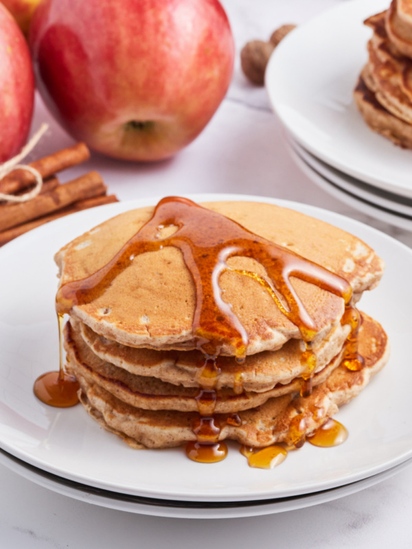 stack of apple pie pancakes with syrup on top on white plate