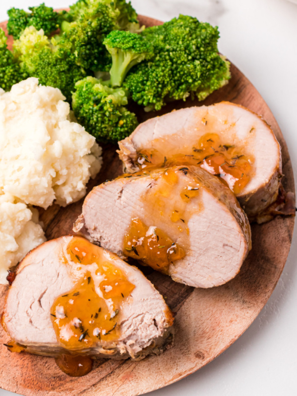 slices of pork roast topped with apricot glaze on plate with potato and broccoli