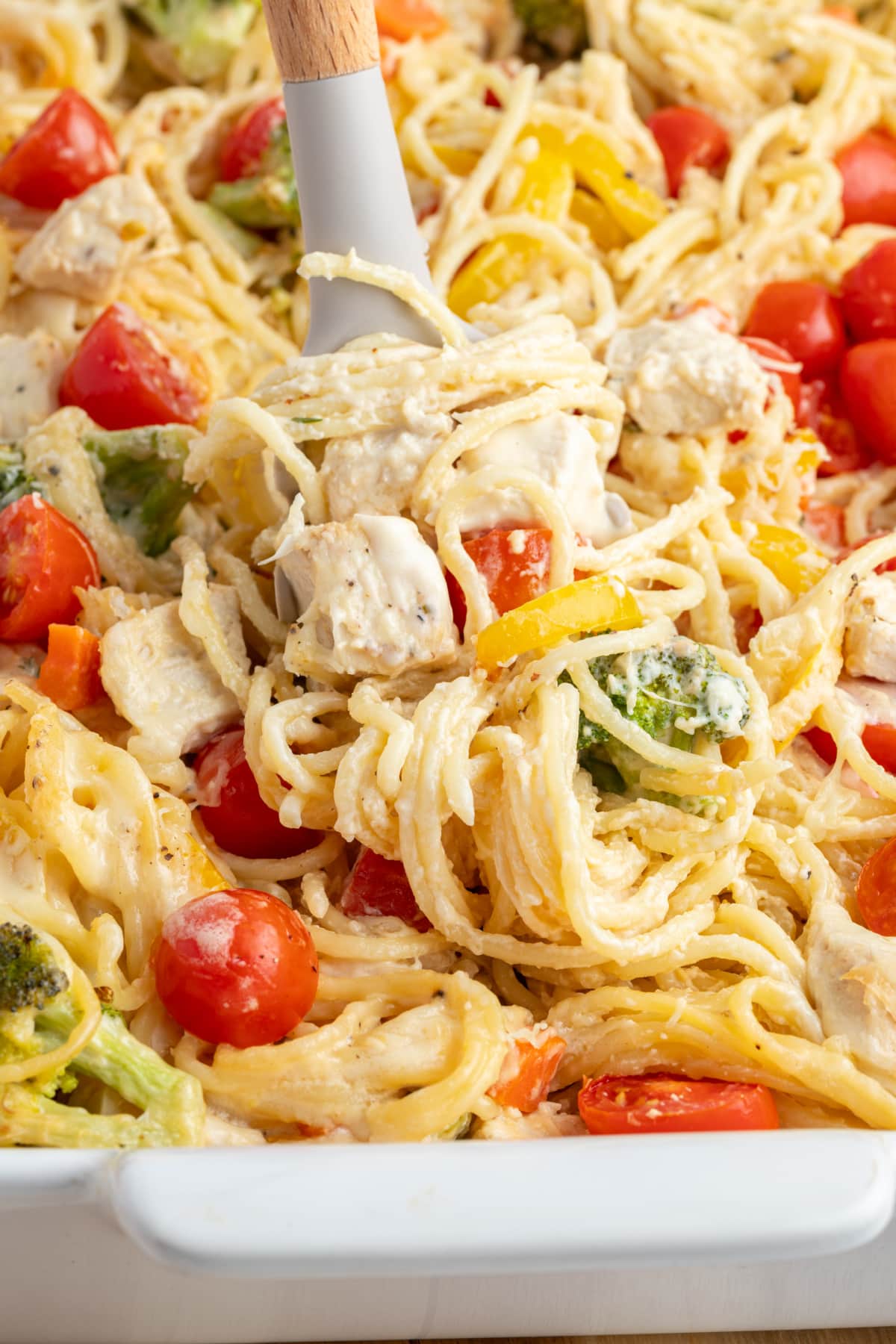 baked lemon chicken spaghetti primavera in baking dish with serving spoon