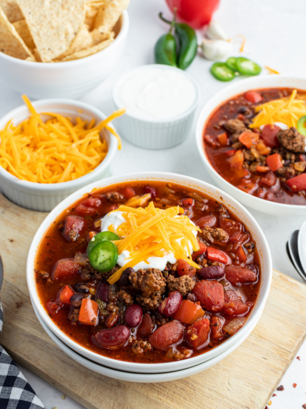 beef and bean chili in a white bowl topped with cheese and sour cream and jalapeno