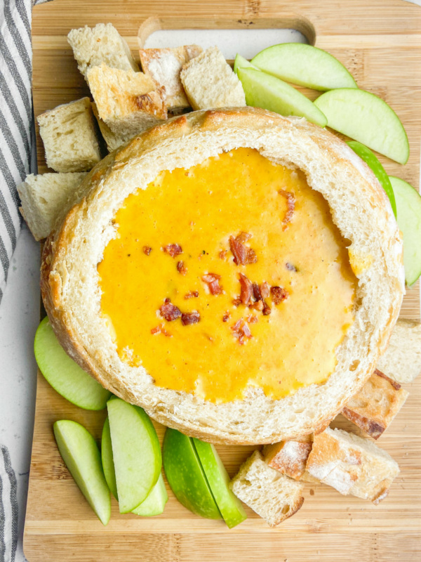 Cheddar Beer Fondue in a bread bowl with apples and bread chunks surrounding