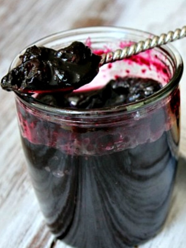 jar of blueberry jam open with a spoon inside and jam on the spoon sitting on the top