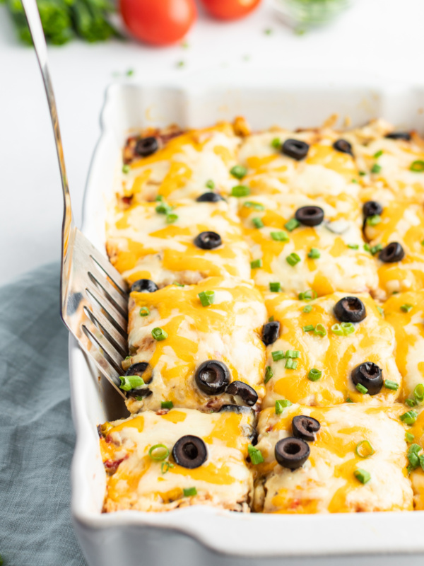 chicken enchilada casserole in a white dish with spatula