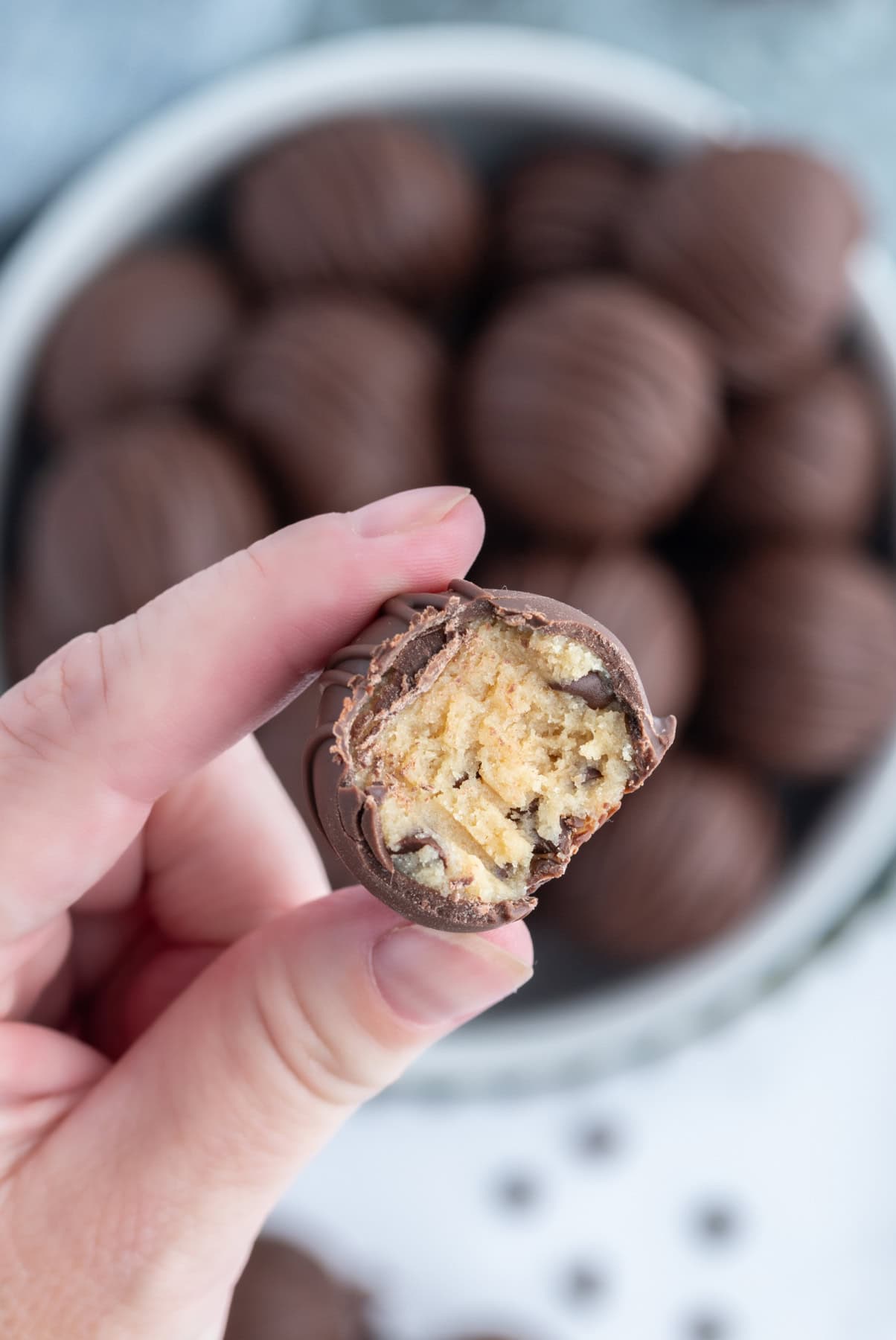 fingers holding a chocolate chip cookie dough truffle with bite taken out