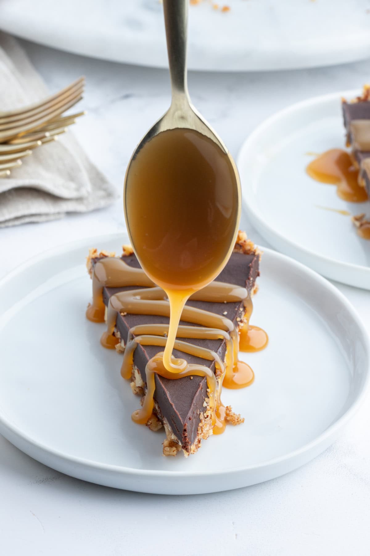 spooning caramel sauce on top of slice of chocolate pecan tart on plate