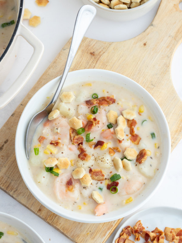 bowl of corn and shrimp chowder with spoon and bacon on top