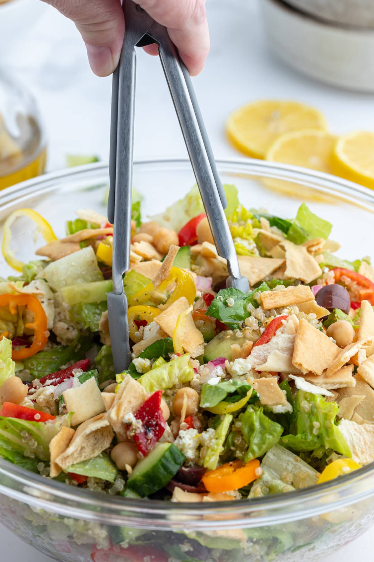 tongs in bowl of greek quinoa chopped salad