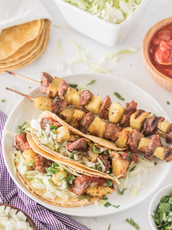 pork and pineapple soft tacos on a plate with kebabs on plate too