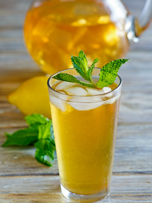 Sweet Summer Iced Tea garnished with mint with a pitcher of iced tea in the background