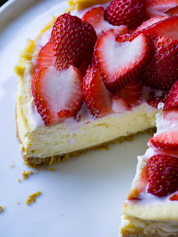 Instant Pot Cheesecake with piece cut out and strawberries on top on white plate