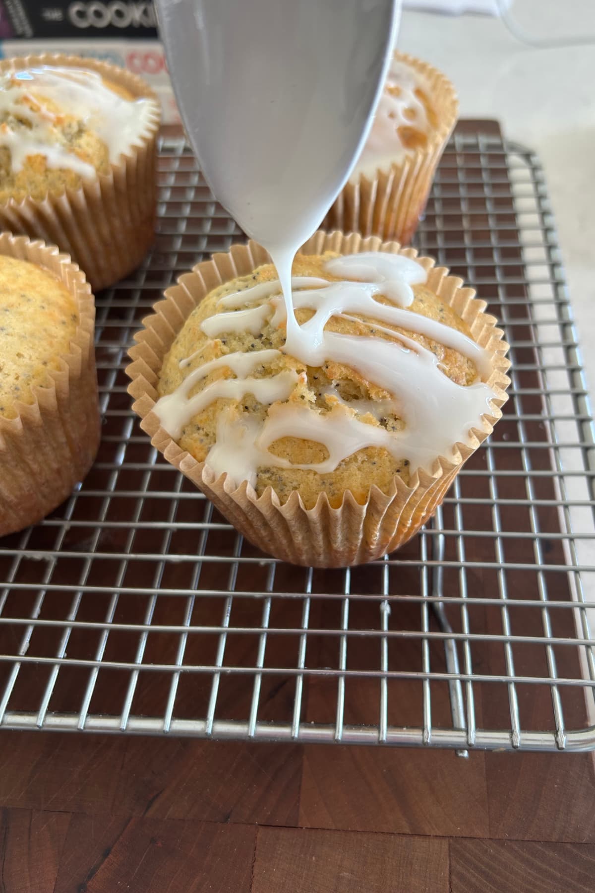 drizzling glaze onto poppy seed muffins on rack