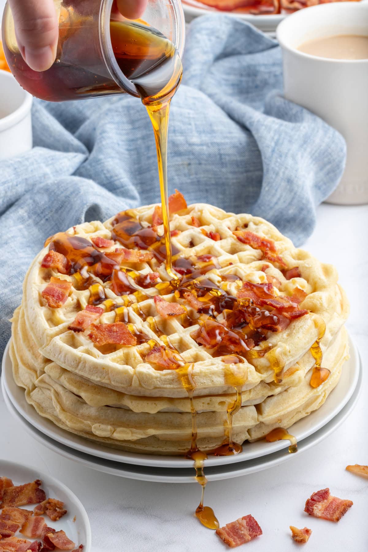 pouring syrup onto stack of maple bacon waffles