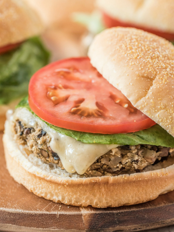 mushroom veggie burger on a wooden board. top of the bun sliding off a bit. tomato and lettuce on the burger too.