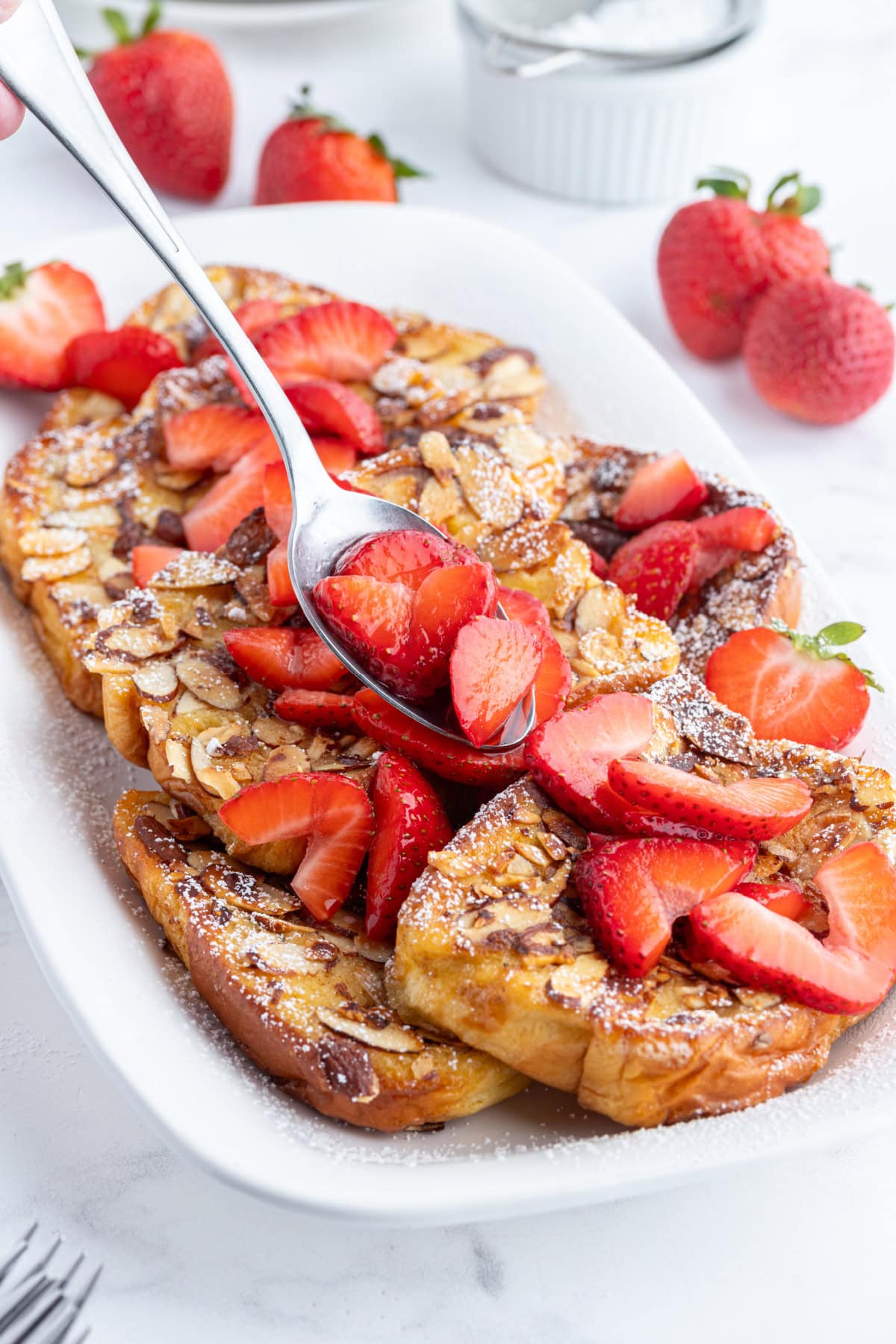 spooning strawberries onto platter of pain perdu