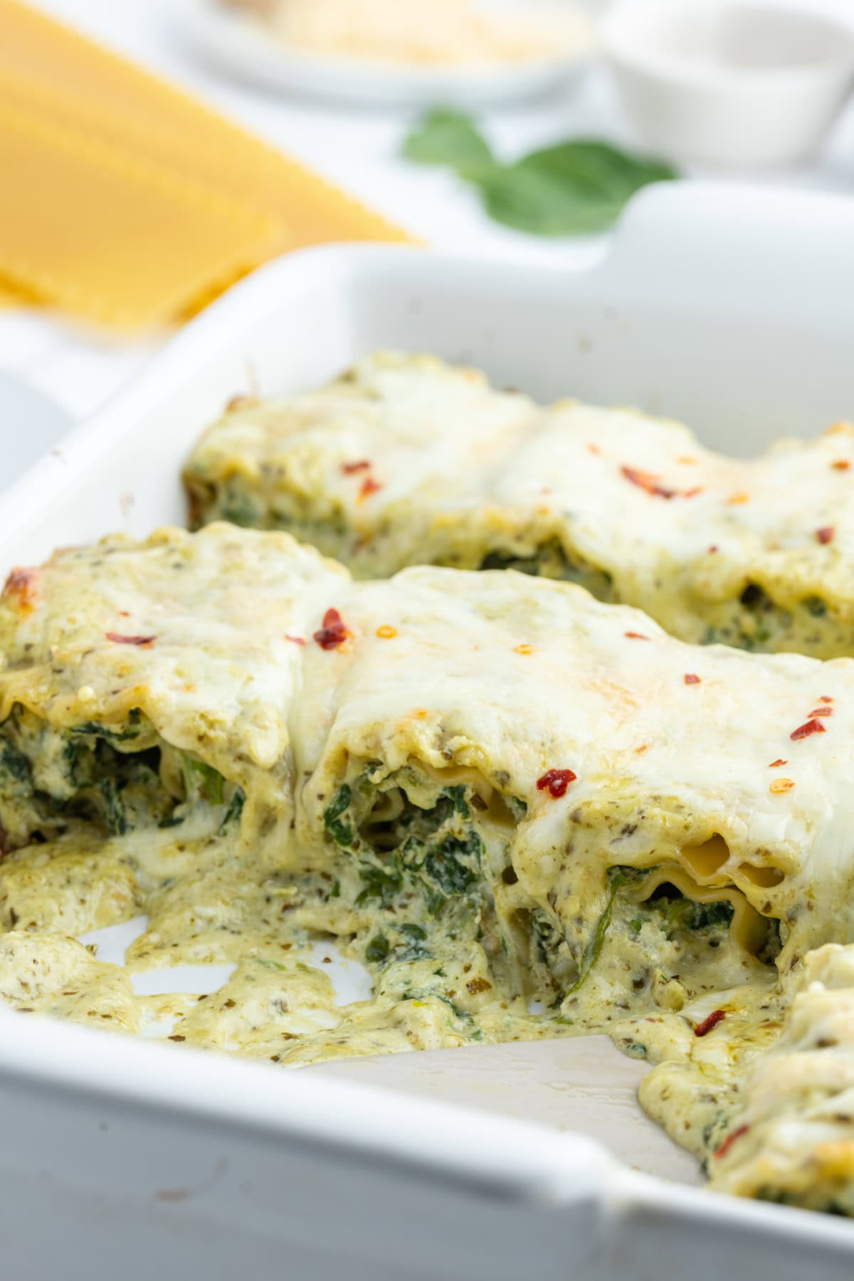 casserole dish of pesto lasagna rolls with some taken out