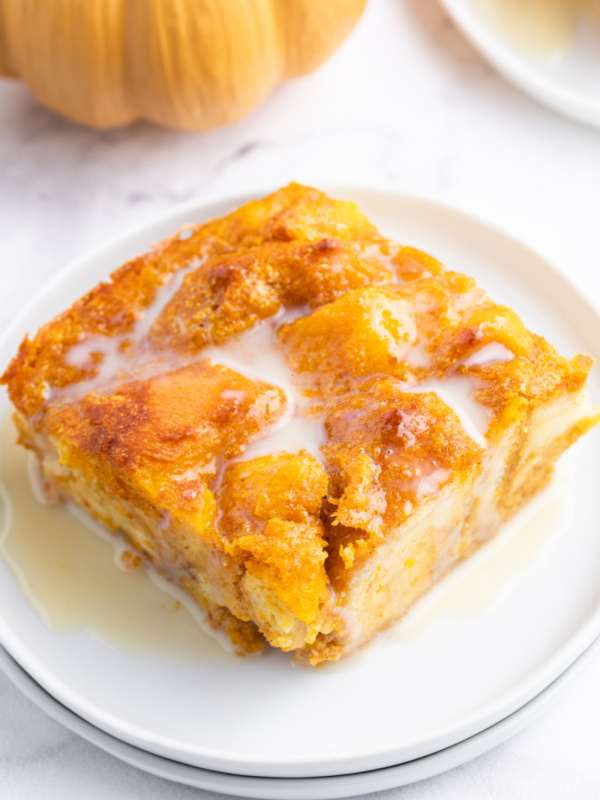 slice of pumpkin bread pudding with bourbon cream sauce on a white plate