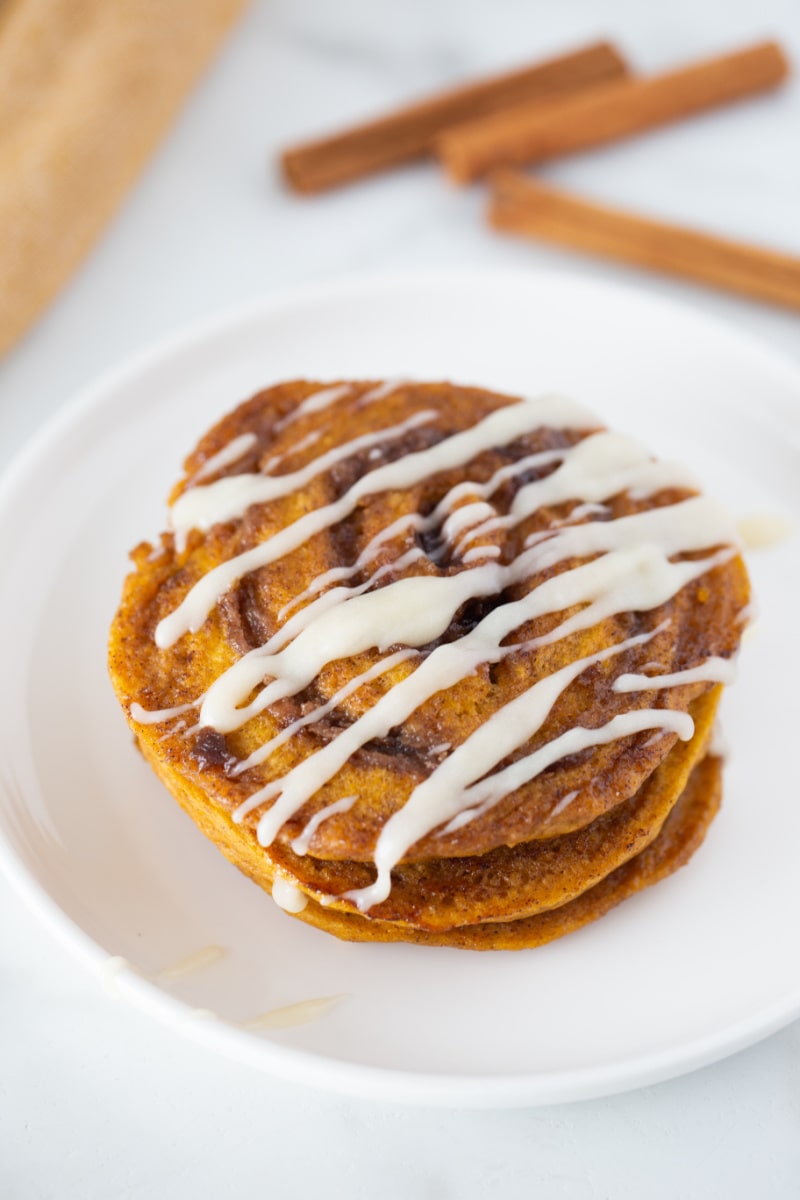 pumpkin cinnamon roll pancakes on plate with cream cheese glaze on top