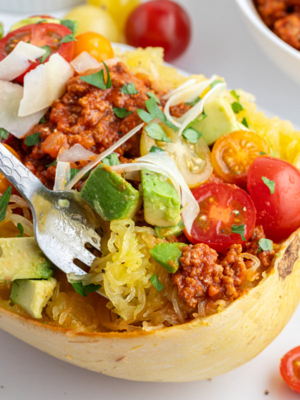 fork in a half spaghetti squash with spicy meat sauce and garnishes