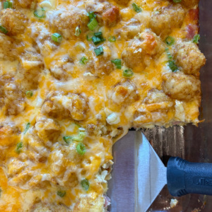 tater tot breakfast casserole in dish with spatula taking out serving