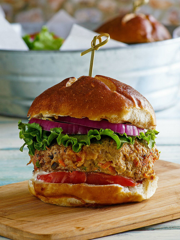 turkey garden burger dressed with lettuce and tomato in a bun with a sandwich pick on top, sitting on a wooden cutting board. galvanized metal tub in background