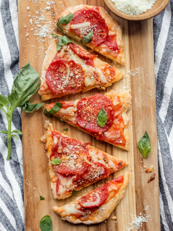 sliced pepperoni pizza on a cutting board garnished with fresh basil set on a white and blue striped napkin