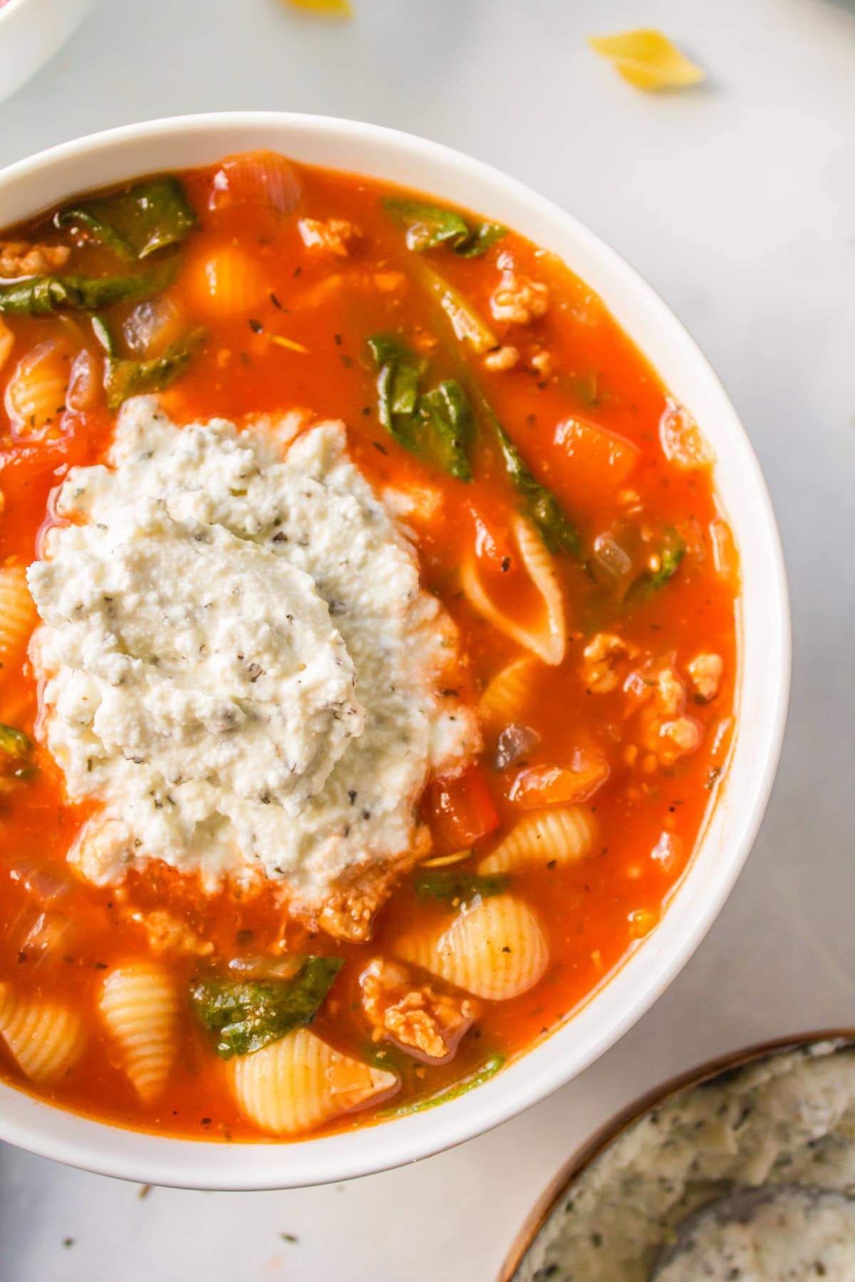 unstuffed shells soup in bowl with spoonful of seasoned ricotta on top