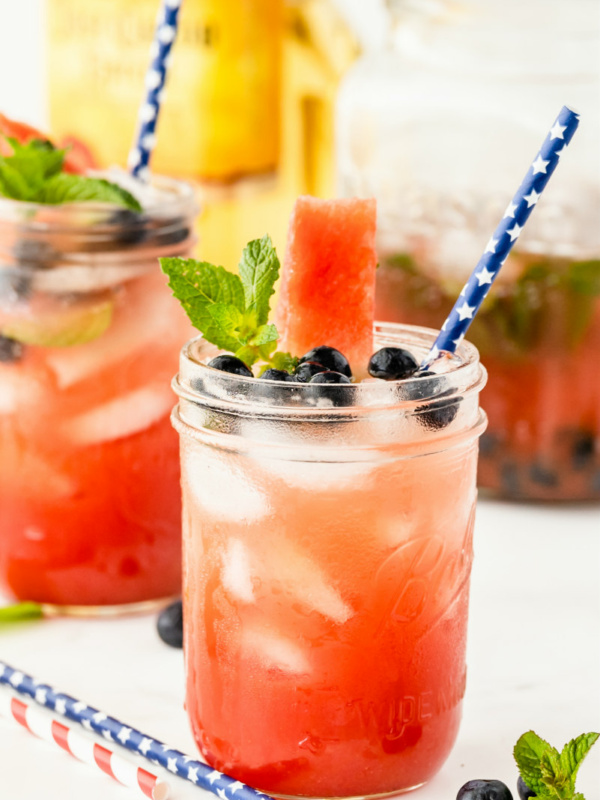 watermelon tequila cocktails in mason jars garnished with fresh blueberries and mint. striped straws. bottle of tequila in the background